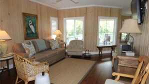 A living room with a sofa, two armchairs, a coffee table, and a TV. - Creekside Cottage (Edisto Island)