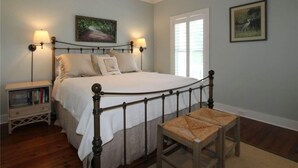 A bedroom with a bed, bedside lamps, a nightstand, and a window. - Creekside Cottage (Edisto Island)