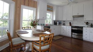 A kitchen with white cabinets, a dining table with chairs, and a stove. - Creekside Cottage (Edisto Island)