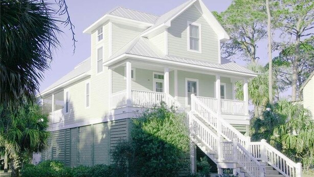 A two-story house with a front porch and a staircase leading to the entrance. - Creekside Cottage (Edisto Island)