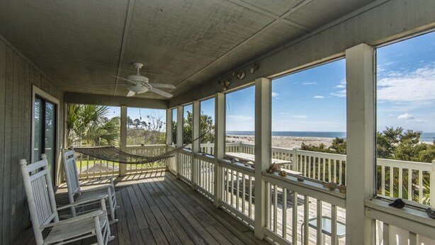 A covered porch with a view of the beach, a ceiling fan, and white rocking chairs. - Crowfield (Edisto Island)