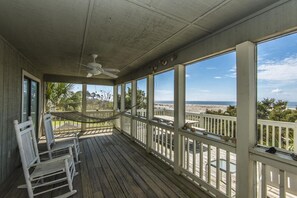 A covered porch with a view of the beach, a ceiling fan, and white rocking chairs. - Crowfield (Edisto Island)