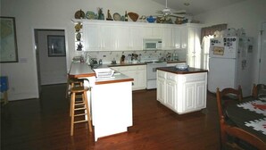 Cucina con mobili bianchi, un forno a microonde, un frigorifero e una ventola a soffitto.