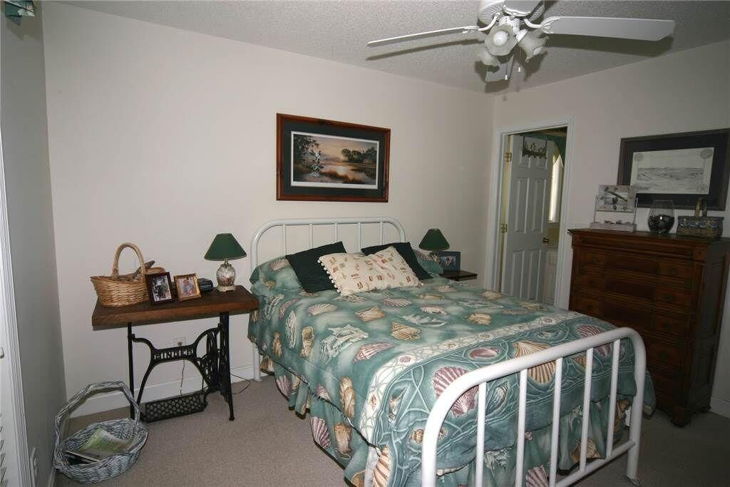 Une chambre à coucher avec un lit, un bureau avec une lampe, une chaise, une commode et un ventilateur de plafond.