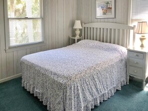 Quarto com cama, mesa de cabeceira, luminária e janela com persianas.