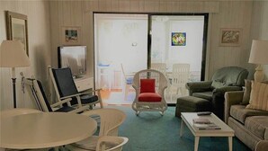 Olohuoneessa on televisio, ruokapöytä tuoleineen, punainen nojatuoli, vihreä nojatuoli ja beigenvärinen sohva.