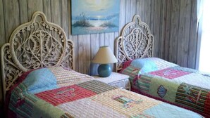 A room with two ornate wooden beds, a small bedside table with a lamp, and a painting on the wall. - Jumangi (Edisto Island)