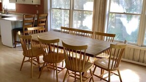 A dining area with a wooden table and chairs, large windows, and a kitchen in the background. - Jumangi (Edisto Island)
