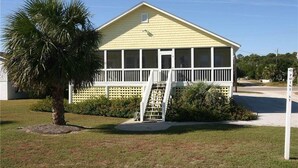 A yellow house with a porch and a staircase leading to the entrance. - Just Sew (Edisto Island)