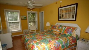A bedroom with a colorful bedspread, a ceiling fan, a nightstand, and a framed picture on the wall. - Just Sew (Edisto Island)