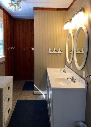 Un bagno con rivestimenti in legno, un lavandino bianco con specchio e uno scaffale con oggetti decorativi.