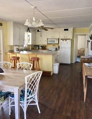Una cucina compatta con mobili bianchi, un'isola centrale con sgabelli, un forno a microonde e un frigorifero.