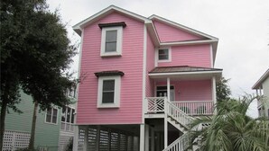 A two-story pink house with a white porch and a staircase leading to the second floor. - Pink Flamingo (Edisto Island)