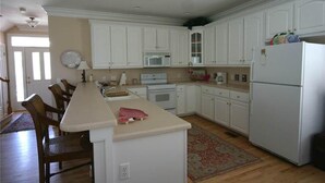 A kitchen with white cabinets, a microwave, a refrigerator, and a dining area with chairs. - Pink Flamingo (Edisto Island)