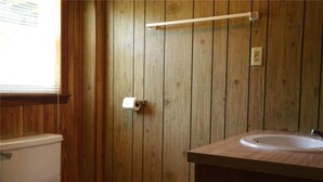 Une salle de bain avec des lambris en bois, des toilettes, un lavabo et un porte-serviettes.