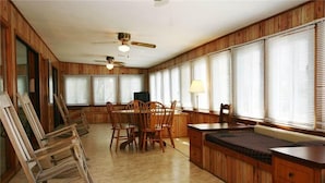 A spacious room with a wooden interior, a dining table with chairs, a bench, and a ceiling fan.