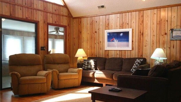 A cozy living room with wooden paneling, a sofa, two armchairs, a coffee table, and two lamps.