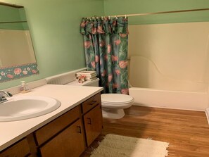 A bathroom with a white sink, wooden cabinets, a toilet, and a shower curtain with a floral pattern. - 1017 Byrd St (Edisto Island)