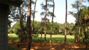 Näkymä golfkentälle, jossa on korkeita puita ja taustalla näkyy rakennus.