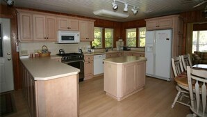 A kitchen with wooden cabinets, a central island, a microwave, a stove, and a refrigerator. - Sound Pleasures (Edisto Island)