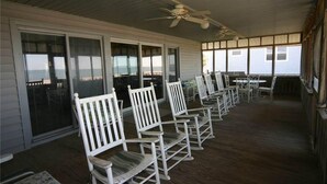 A covered porch with white rocking chairs and a ceiling fan. - Sound Pleasures (Edisto Island)