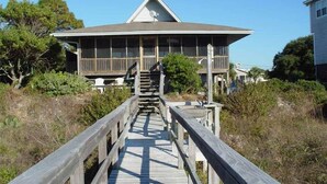 A wooden boardwalk leading to a building with a gabled roof and a balcony, surrounded by vegetation. - Sound Pleasures (Edisto Island)