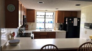 A kitchen with wooden cabinets, a white countertop, a sink, a refrigerator, and a clock on the wall. - Summerwind 782 (Edisto Island)