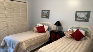 A bedroom with two single beds, a nightstand with a lamp, and a wardrobe. - Summerwind 782 (Edisto Island)