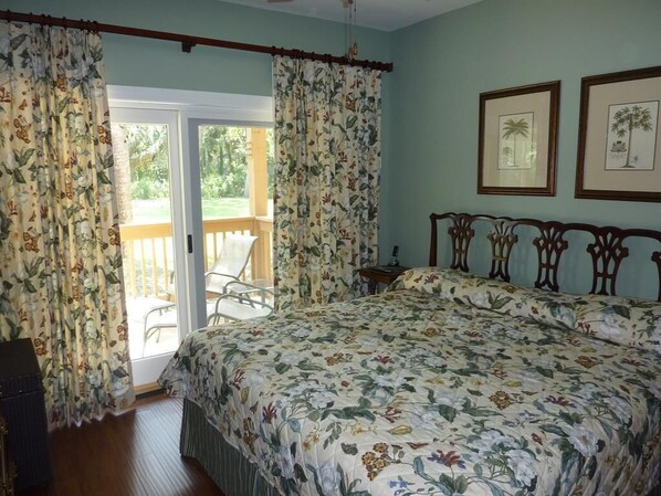 A bedroom with a floral bedspread, a wooden headboard, and a balcony with curtains.
