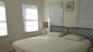A bedroom with a bed, white walls, and a window with blinds. - Top Gunn (Edisto Island)