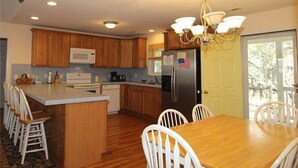 A kitchen with wooden cabinets, a central island, white chairs, a dining table, a refrigerator with an American flag, and a chandelier.