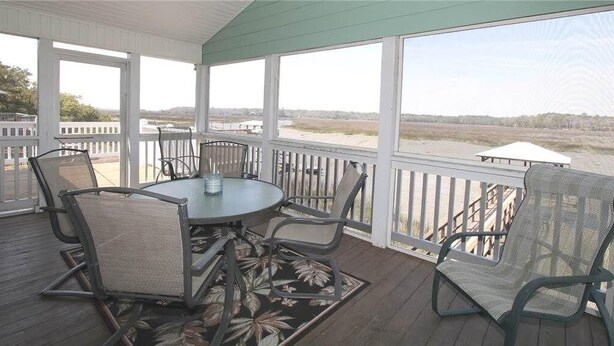 A covered outdoor area with a table and chairs, a view of the beach, and a white railing.