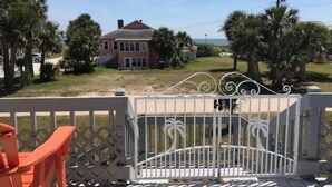 A wooden deck with a white metal railing, overlooking a residential area with houses and palm trees. - A Shore Investment (Edisto Island)