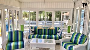 A covered patio area with wicker furniture, a glass coffee table, and a view of the outdoors. - A Shore Investment (Edisto Island)