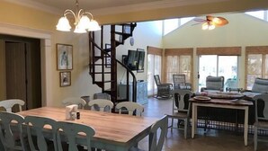 A spacious dining area with a wooden table and chairs, a staircase, and a seating area with chairs and a small table. - A Shore Investment (Edisto Island)
