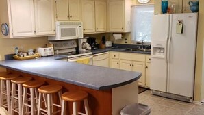 Une cuisine dotée d’un îlot central, de tabourets en bois, d’un four à micro-ondes, d’un réfrigérateur et d’une poubelle.