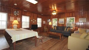 A wooden-paneled room with a dining table, sofa, and television. - Anchor inn (Edisto Island)