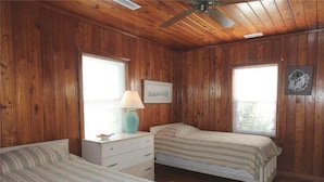 A wooden-paneled bedroom with two beds, a nightstand, a lamp, and a framed picture on the wall. - Anchor inn (Edisto Island)