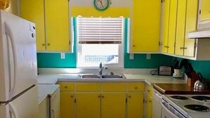 A kitchen with yellow cabinets, a white refrigerator, a sink, and a stove. - Beach Retreat (Edisto Island)