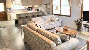 Uma sala de estar com sofá, mesa de centro e televisão. Há também uma área de cozinha com armários e micro-ondas.