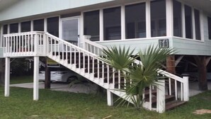 Uma casa de dois andares com fachada branca, varanda frontal e grade branca, e escadaria que leva ao andar superior.