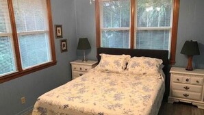 Quarto com uma cama, duas mesas de cabeceira, duas luminárias e duas janelas com persianas.