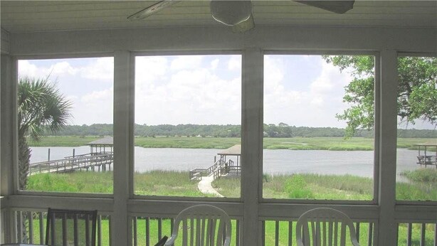 A covered outdoor area with a table and chairs, overlooking a body of water and a dock. - Dreamcatcher (Edisto Island)