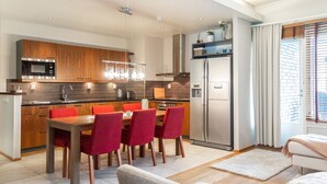 A modern kitchen with wooden cabinets, a stainless steel refrigerator, and a dining area with red chairs.