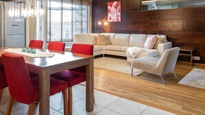 A modern living room with a sofa, a dining table with chairs, and a wooden floor.