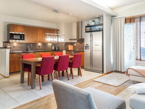 A modern kitchen with a dining area, featuring a stainless steel refrigerator, wooden cabinets, and a red dining set.