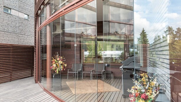 A modern outdoor deck with glass walls, wooden flooring, and outdoor furniture.