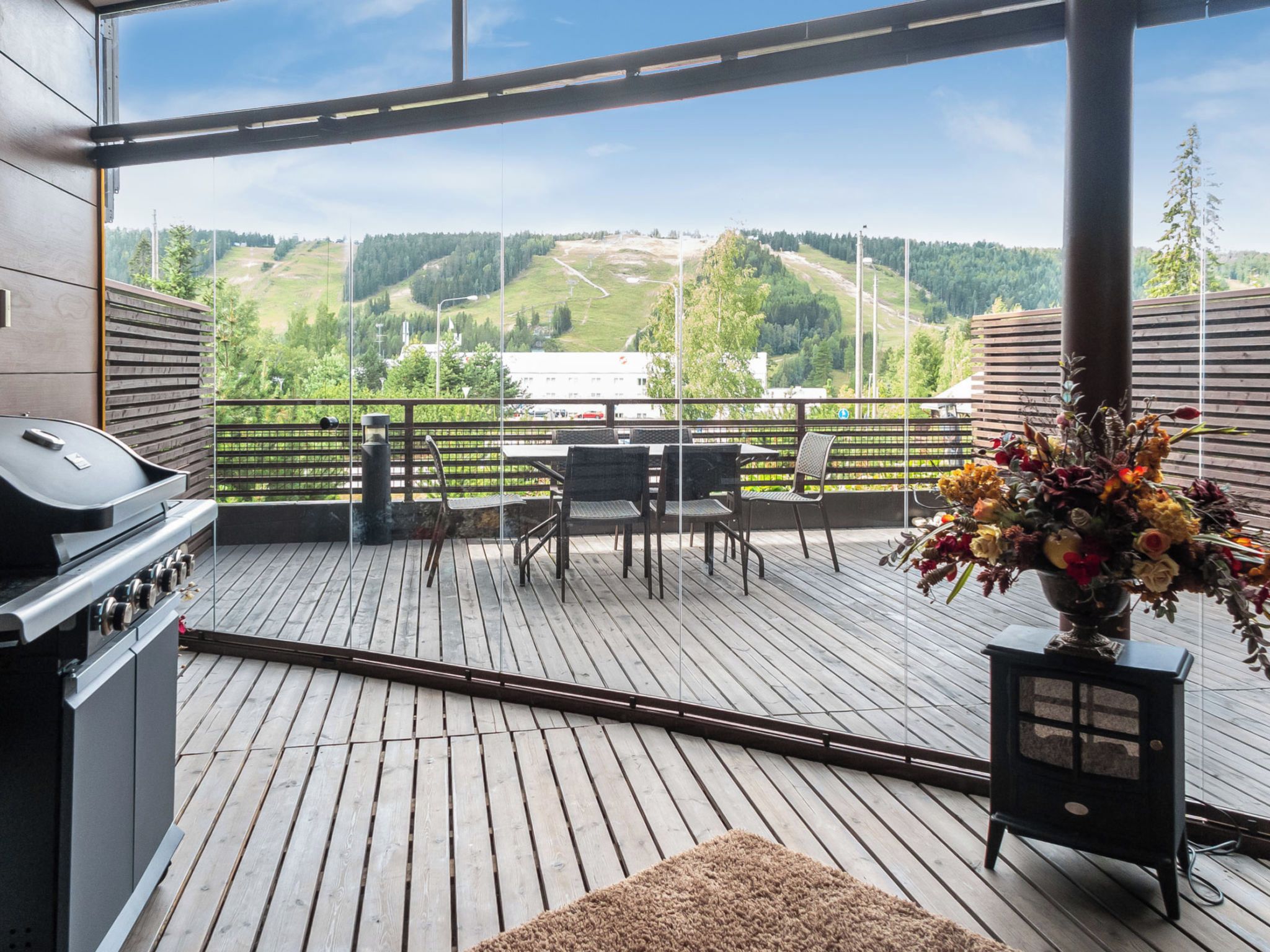 A balcony with a view of a green landscape, a grill, and a table with chairs.