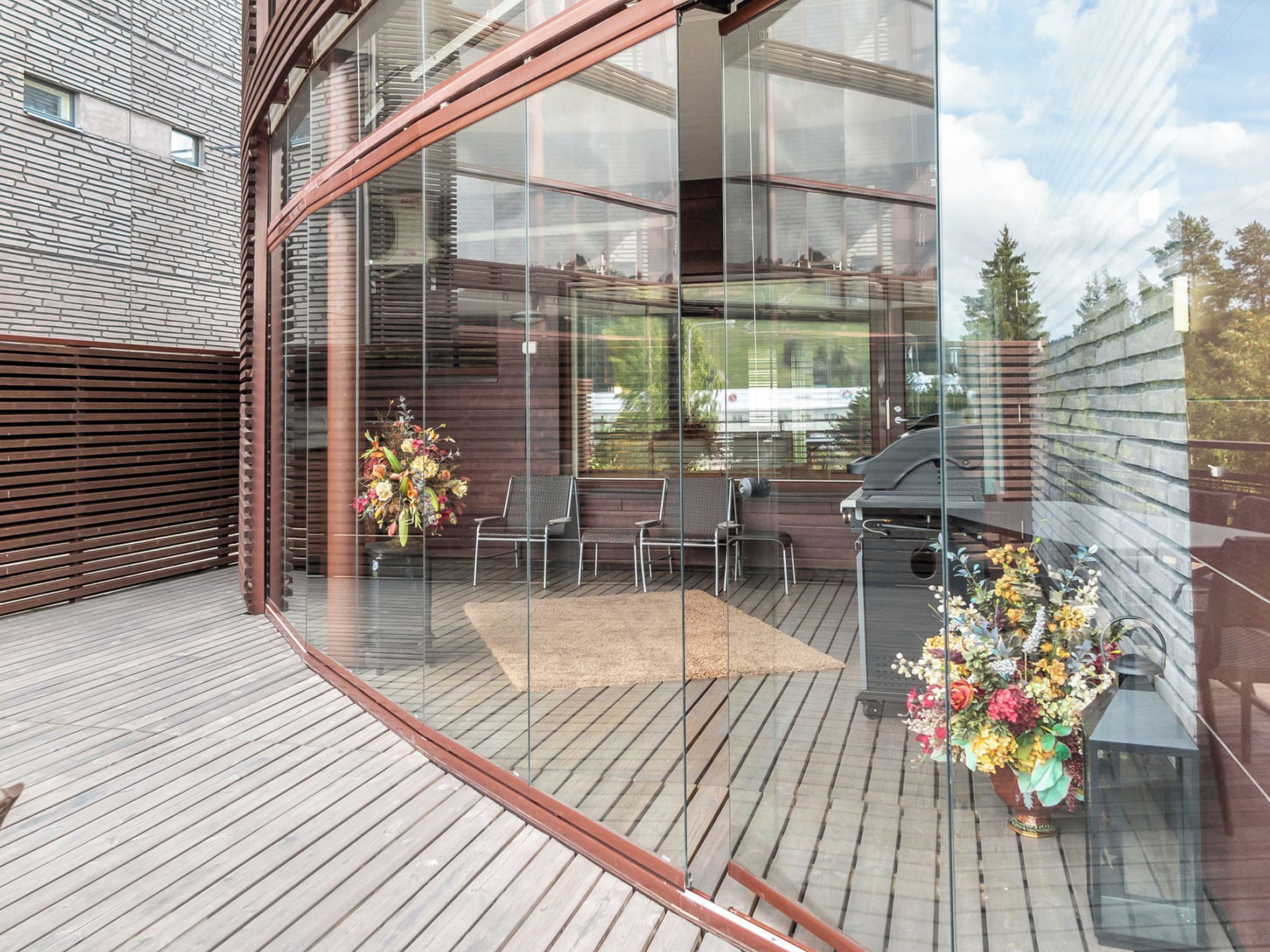 A modern outdoor deck with glass walls, wooden flooring, and outdoor seating.