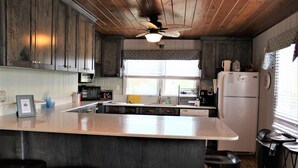 Una cucina con mobili in legno, un'isola centrale con sgabelli, un frigorifero e una ventola a soffitto.